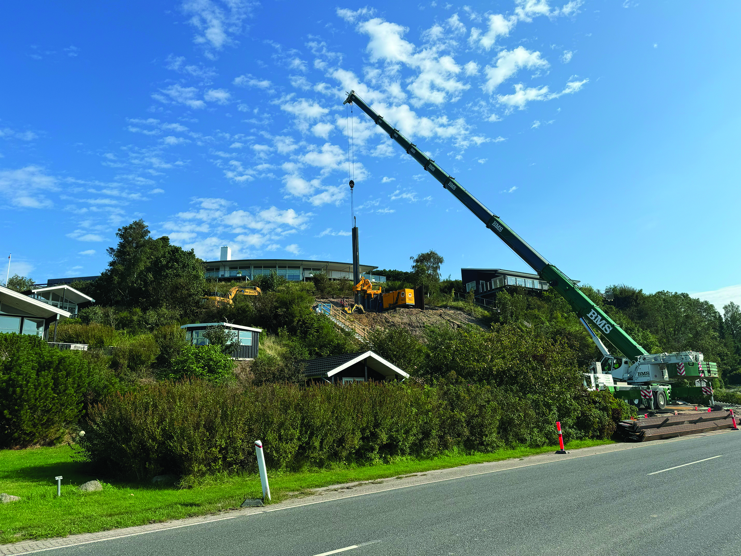 Crane lifting sheet piles into a Kowan Silent Sheet Piling Press up a hill
